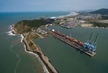 Vista aérea do porto de Imbituba, em Santa Catarina, com navios, guindastes e estruturas de movimentação de cargas.