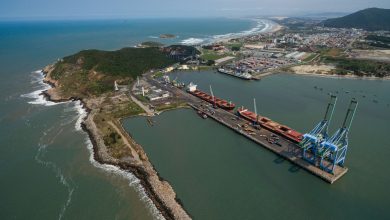 Vista aérea do porto de Imbituba, em Santa Catarina, com navios, guindastes e estruturas de movimentação de cargas.