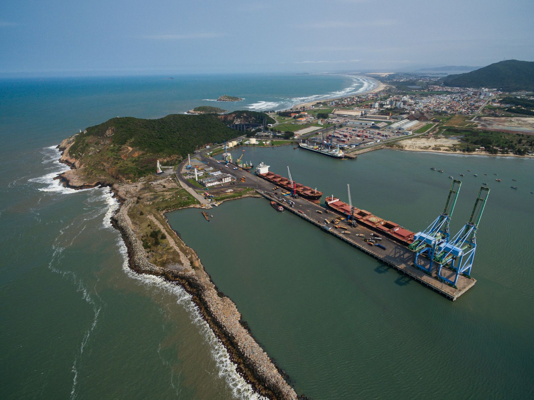 Vista aérea do porto de Imbituba, em Santa Catarina, com navios, guindastes e estruturas de movimentação de cargas.