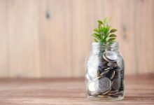 Pote transparente com moedas e uma pequena planta, simbolizando investimento e crescimento sustentável.