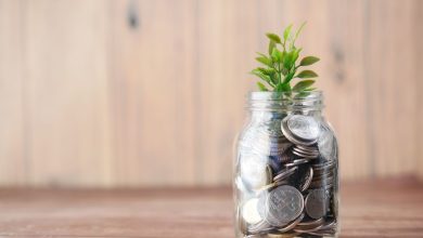 Pote transparente com moedas e uma pequena planta, simbolizando investimento e crescimento sustentável.